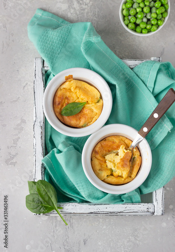 Canvastavla Cheese souffle with green peas in a white ceramic ramekin on a white wooden tray