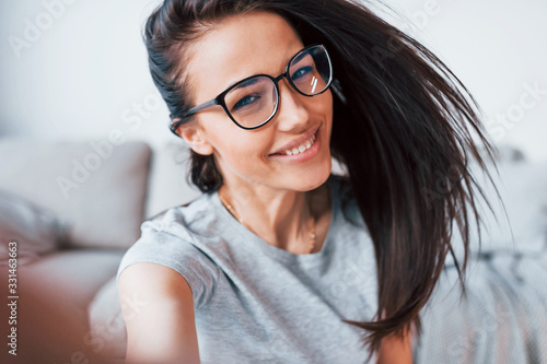 Making selfie. Young beautiful woman in casual clothes and glasses have fun at home alone