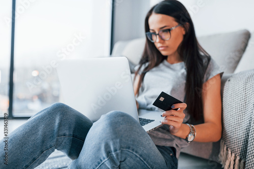 Young beautiful woman in casual clothes sitting at home alone with laptop and credit card