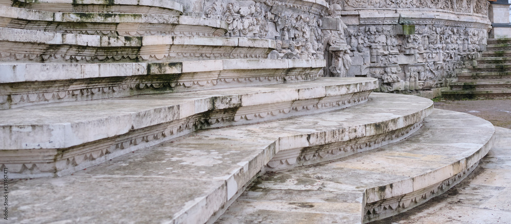 Old steps of white stone covered with mold running along a stone wall with bas-relief. Old steps of white stone covered with mold running along a stone wall with bas-relief.