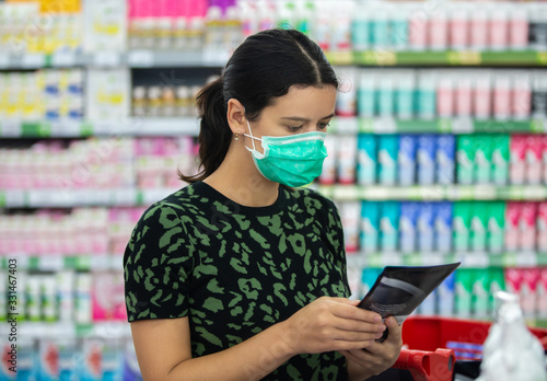 Young woman wears medical mask against coronavirus while shopping in supermarket or store- health, safety and pandemic concept - protective medical mask for protection from virus covid-19
