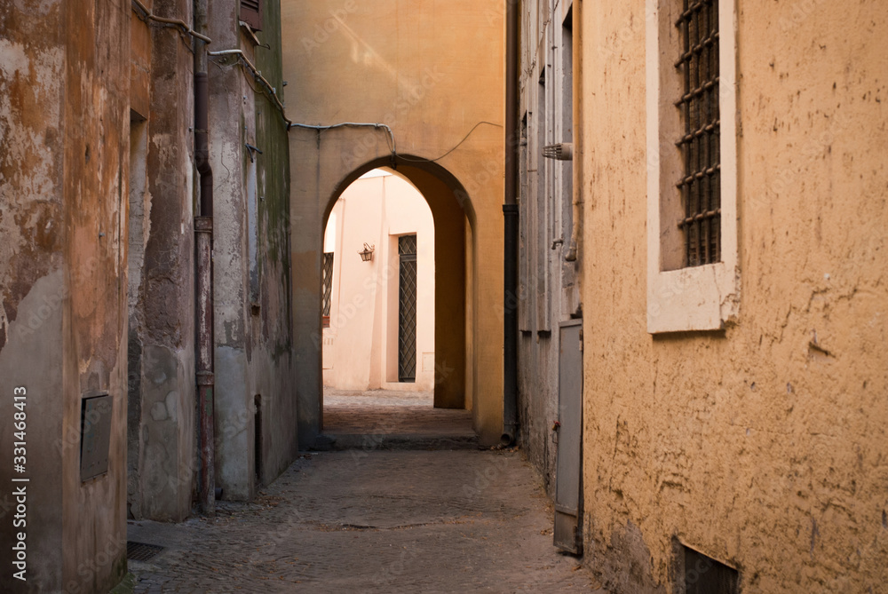 A city street without people. A narrow street with yellow houses and an arch in the middle.