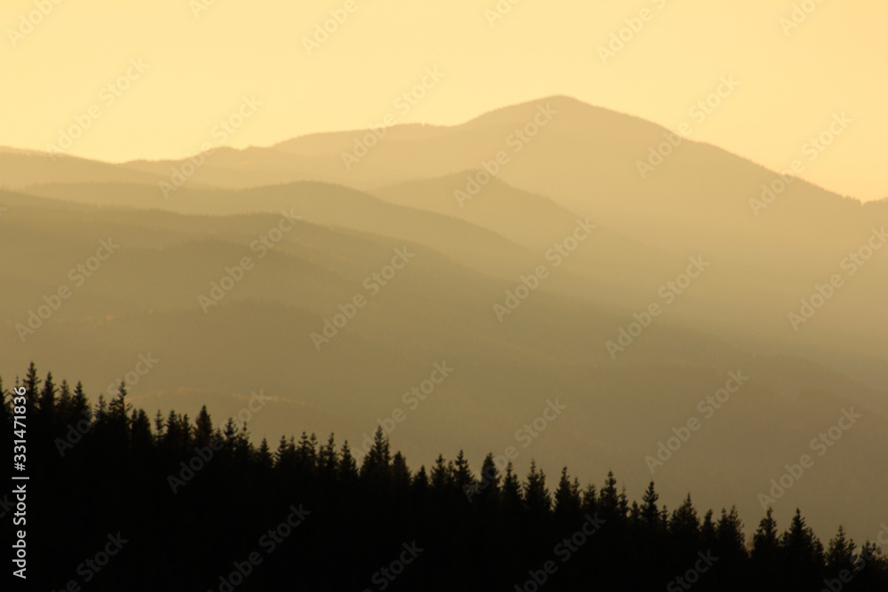 Warm gradient of dawn sky above layers of mountain and rock silhouettes. Vivid alpine landscape with dark rockies and orange sunrise sky. Minimalist highland scenery with silhouette of rocky mountains