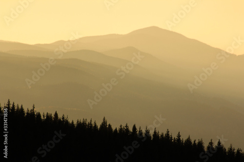 Warm gradient of dawn sky above layers of mountain and rock silhouettes. Vivid alpine landscape with dark rockies and orange sunrise sky. Minimalist highland scenery with silhouette of rocky mountains