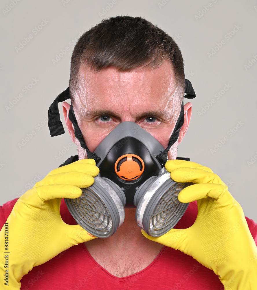 Portrait of young man in gloves wearing respirator over gray background Portrait of young man in gloves wearing respirator over gray background