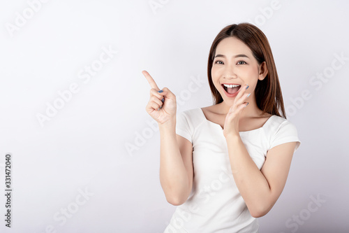Asian pretty woman in white t-shirt and white pants pretending to point with copy space on white background. Information telling, shopping promotion, announcement, selling support concept.