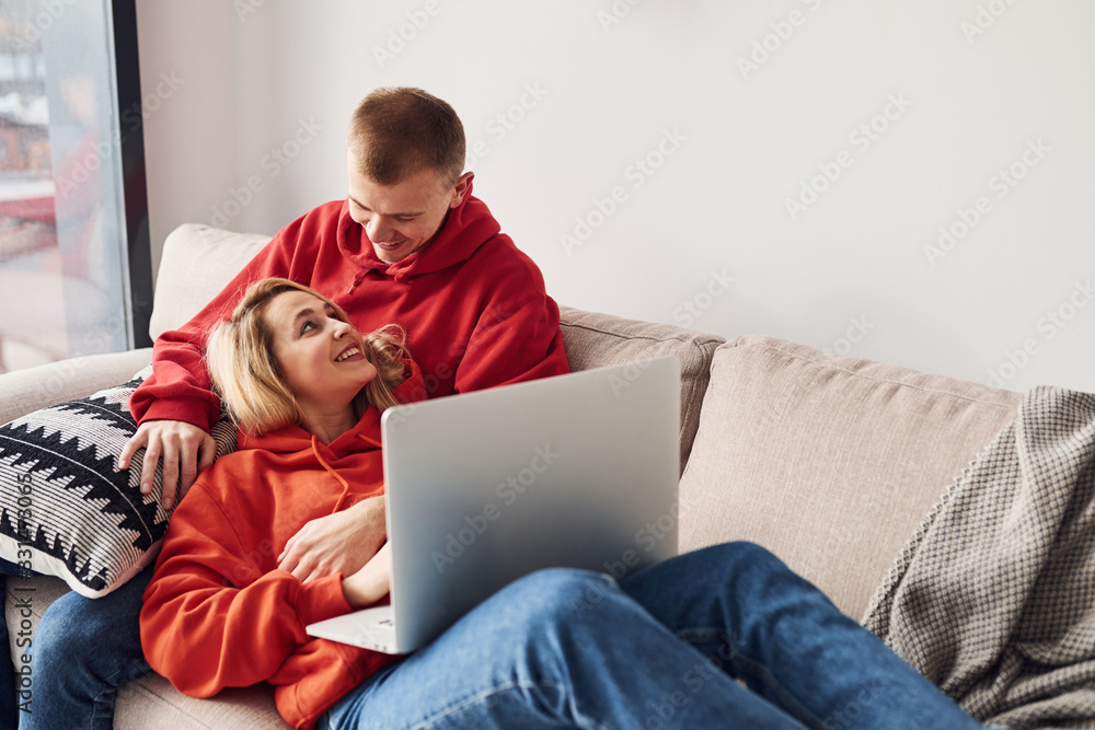 Using laptop that is on the legs. Young lovely couple together at home spending weekend and holidays together Using laptop that is on the legs. Young lovely couple together at home spending weekend and holidays together