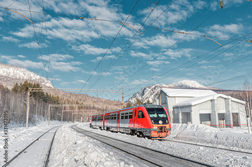 High speed passenger train passes near a station in the winter mountains