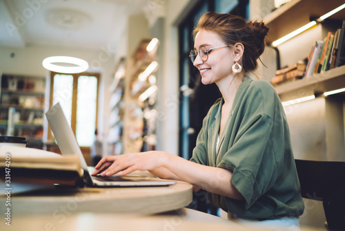 Cheerful young freelance woman typing on laptop in library photo