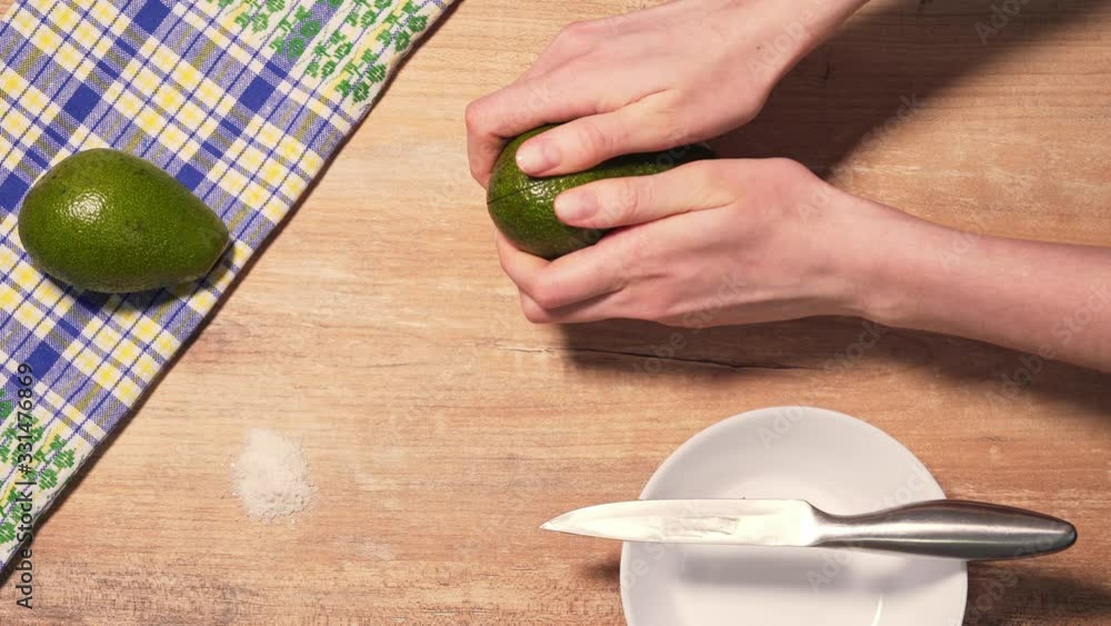 Female hands reveal 2 halves of ripe avocado on a wooden table background, top view Female hands reveal 2 halves of ripe avocado on a wooden table background, top view