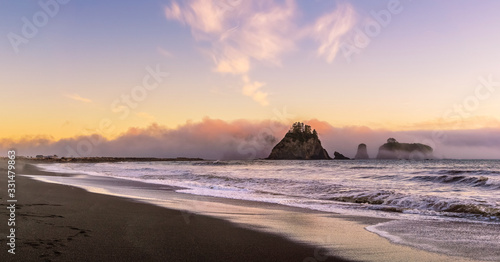 Rialto Beach at dusk with sea stacks covered with clouds coming from the ocean, Olympic National Park, Washington state, USA.