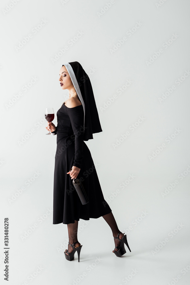 attractive sensual nun holding glass and bottle of wine on grey attractive sensual nun holding glass and bottle of wine on grey