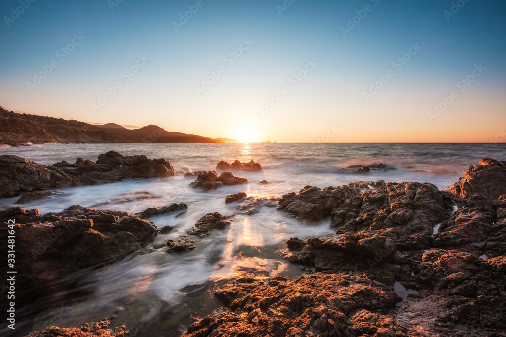 Waves washing onto rocky Corsica coastline at sunset