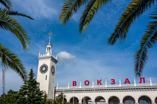 Russia, Black Sea, Sochi: Central railway station main building (Vokzal) in the city center of the Russian town with high clock tower, blue sky in the background - public transport travel destination