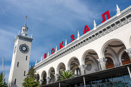 Russia, Black Sea, Sochi: Central railway station main building (Vokzal) in the city center of the Russian town with high clock tower, blue sky in the background - public transport travel destination