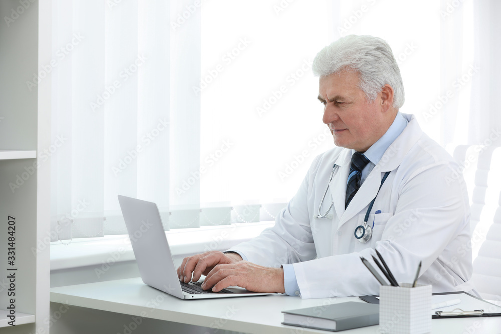 Senior doctor working with laptop at table in office Senior doctor working with laptop at table in office