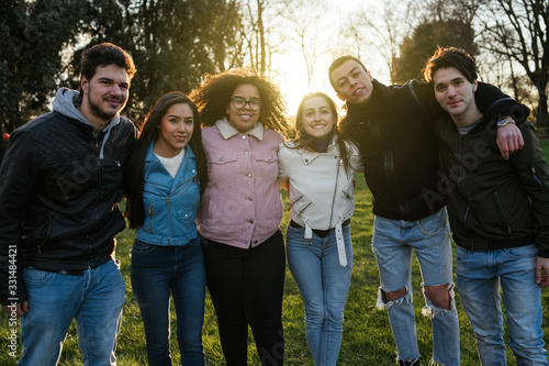 Group of teenagers of different cultures hugging each other at the park - Teamwork of young people forming a semicircle - Six men and women having fun together