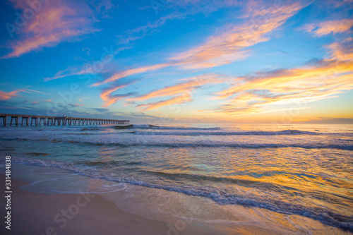 sunset sky and clouds over ocean waves at beach with pier in background