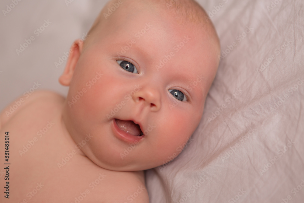 Happy 3 months old baby smiling, lying on white bed