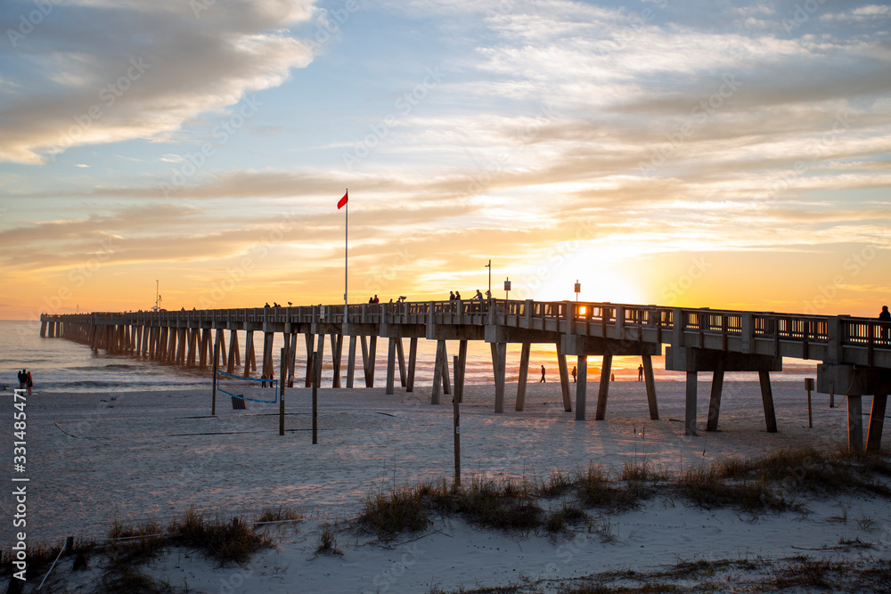 sunset at panama city beach pier with sun going down behind pier and beautiful clouds and sky and ocean