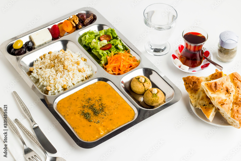 Ramadan iftar meal with soup,rice with chicken chickpea,vegetable salad,dessert and dry fruits in the stainless steel,portion food tray.Top view,fulled frame.