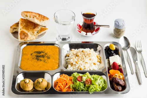 Ramadan iftar meal with soup,rice with chicken chickpea,vegetable salad,dessert and dry fruits in the stainless steel,portion food tray.Top view,fulled frame.