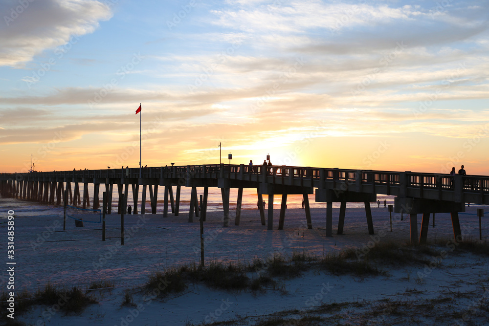 sunset at panama city beach pier with sun going down behind pier and beautiful clouds and sky and ocean