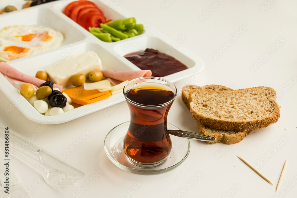 Traditional Turkish breakfast with cheese, salami, pepper, jam, egg, tomato and olives in a plastic white food tray (table d'hote) on white Traditional Turkish breakfast with cheese, salami, pepper, jam, egg, tomato and olives in a plastic white food tray (table d'hote) on white