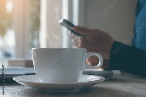 Cup of black coffee and man using smartphone