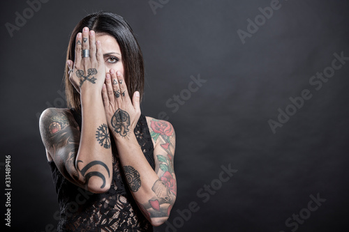 Ragazza tatuata morasi portale mani in faccia , isolata su sfondo nero photo