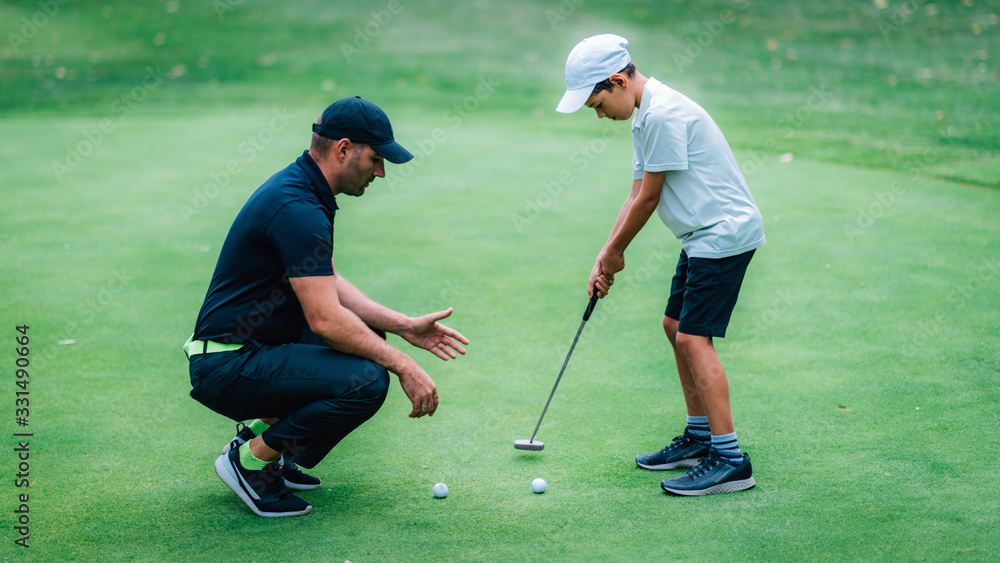 Obraz premium Golf Putting Training. Golf Instructor with Young Boy Practicing on the Putting Green