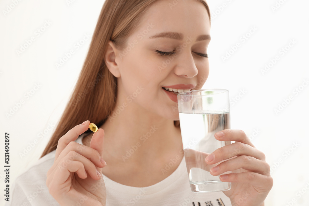 Young woman with glass of water taking vitamin capsule on light background Young woman with glass of water taking vitamin capsule on light background