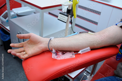 Arm on an armrest, hypodermic needle, tubes, container with blood. Taking blood from the vain of a donor © Yurii Zushchyk