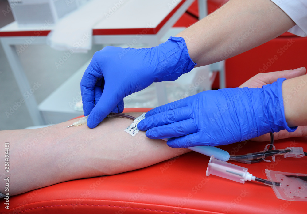 Nurse hands in blue gloves taking blood from the vain of donor with hypodermic needle