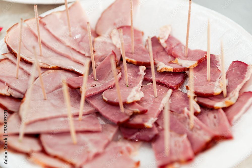 Thin slices of meat, ham, bacon lie on a white plate.
