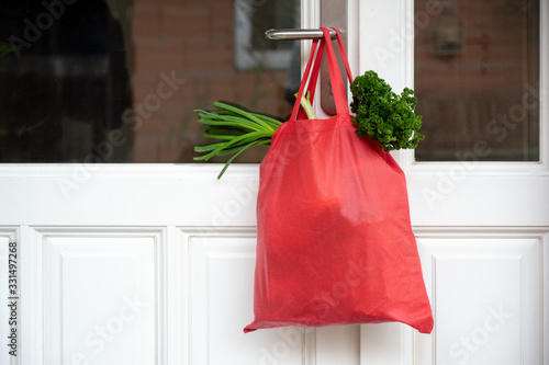 Shopping bag with goods and food is hanging at the front door, neighborhood help concept at quarantine time because of coronavirus infection, copy space