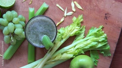 Celery juice spinning on wooden plate composed of nutritious fruits and ingredients such as apples, grapes and lime.
