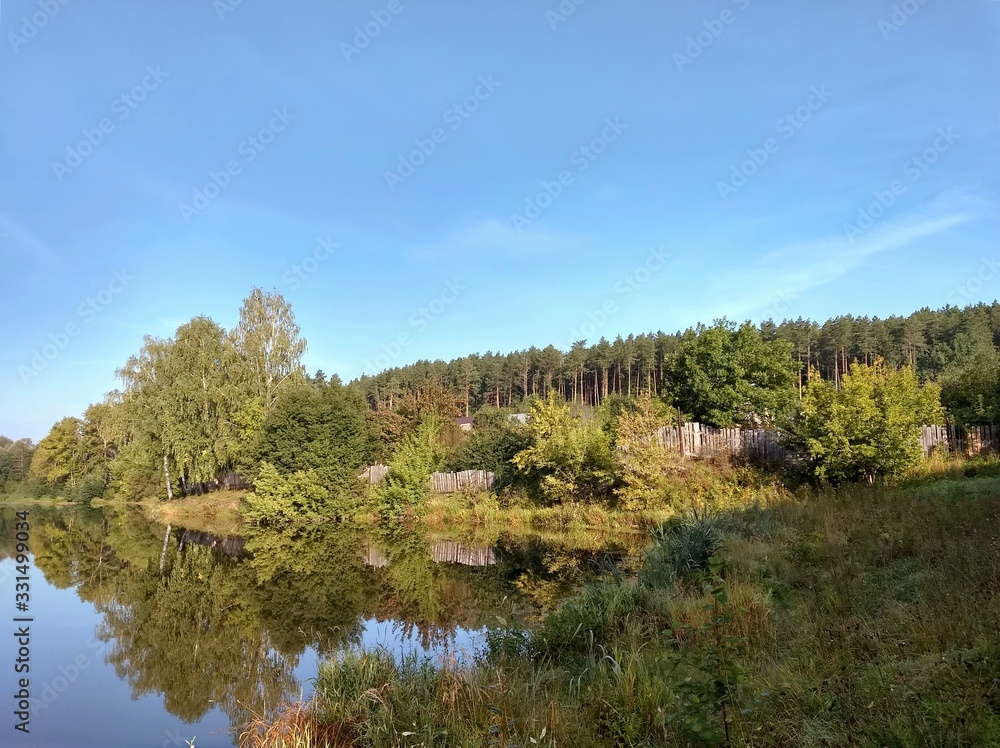 beautiful warm landscape by a pond with trees and a fence, reflected in the water