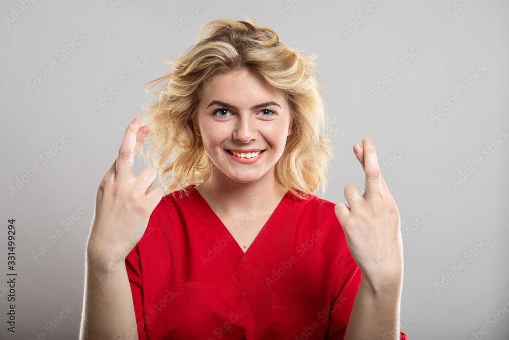 Portrait of female nurse wearing red scrub holding fingers crossed Portrait of female nurse wearing red scrub holding fingers crossed