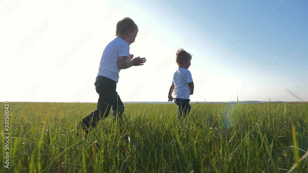 Two children in white t-shirts running on green fresh grass. Happy children enjoy life. The concept of teamwork. Two children in white t-shirts running on green fresh grass. Happy children enjoy life. The concept of teamwork.