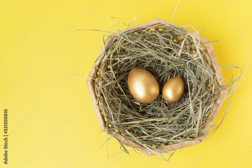 Golden eggs in the wicker basket with hay on the yellow background.Happy Easter. Top view. Flat lay. Copy space. Place for text and design. Golden eggs in the wicker basket with hay on the yellow background.Happy Easter. Top view. Flat lay. Copy space. Place for text and design.
