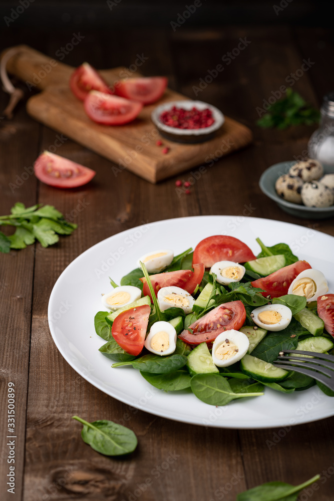 Salad with spinach, cucumber, tomato and quail egg on a white plate on a wooden background. Salad with spinach, cucumber, tomato and quail egg on a white plate on a wooden background.