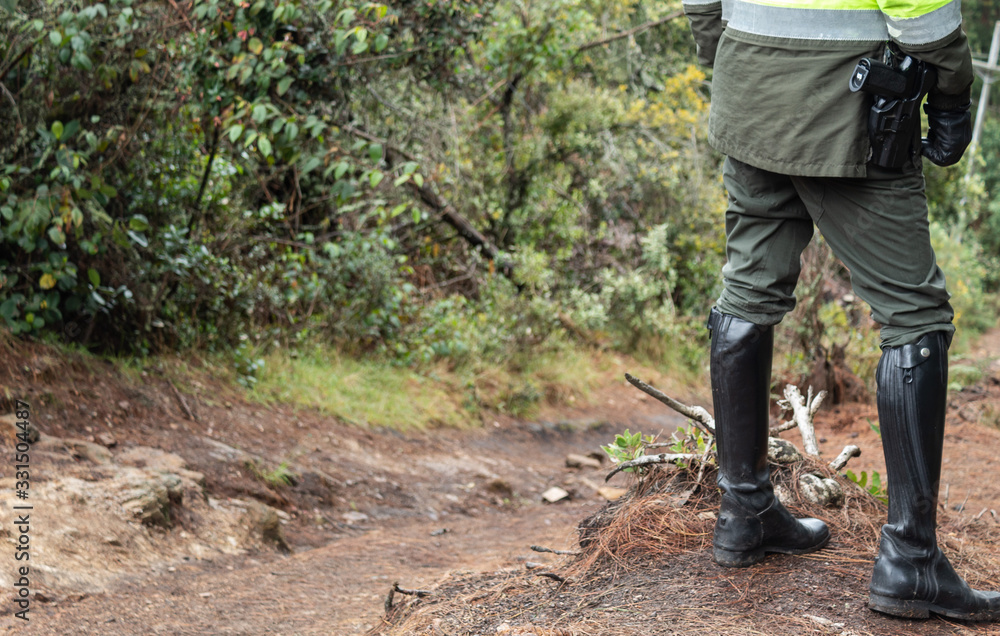 Police Officer wearing a green uniform on duty guarding rural path with black boots and a piston on his waist Police Officer wearing a green uniform on duty guarding rural path with black boots and a piston on his waist