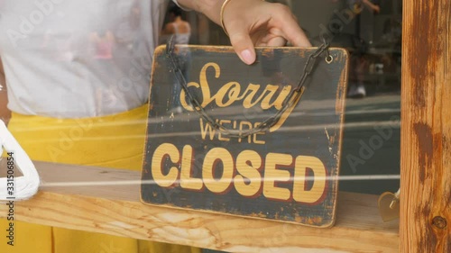 Owner woman set 'closed' sign at window of small shop, indicate break for lunch time or end of workday. Closeup shot of vintage sign plate stick behind window glass