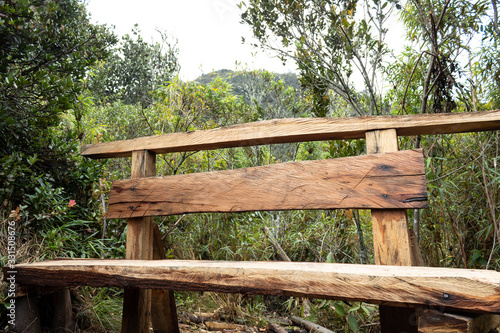 artesanal Wooden bench bank in middle of trekking path at andes mountain near to bogota city with nature and mountains at background in sunny day © Alejandro Bernal