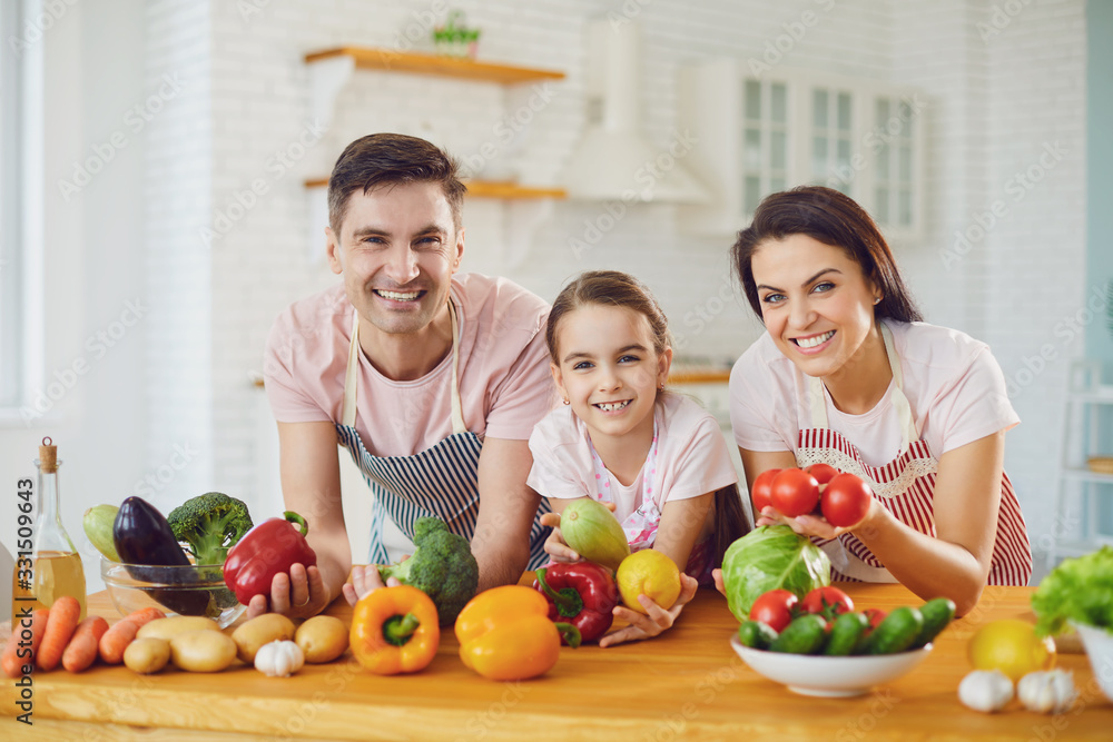 Happy family smiling at a table with fresh vegetables make salad in the kitchen.