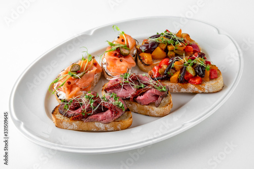 Bruschetta with salmon, capers, grilled vegetables and pork or beef slices. Banquet festive dishes. Gourmet restaurant menu. White background.