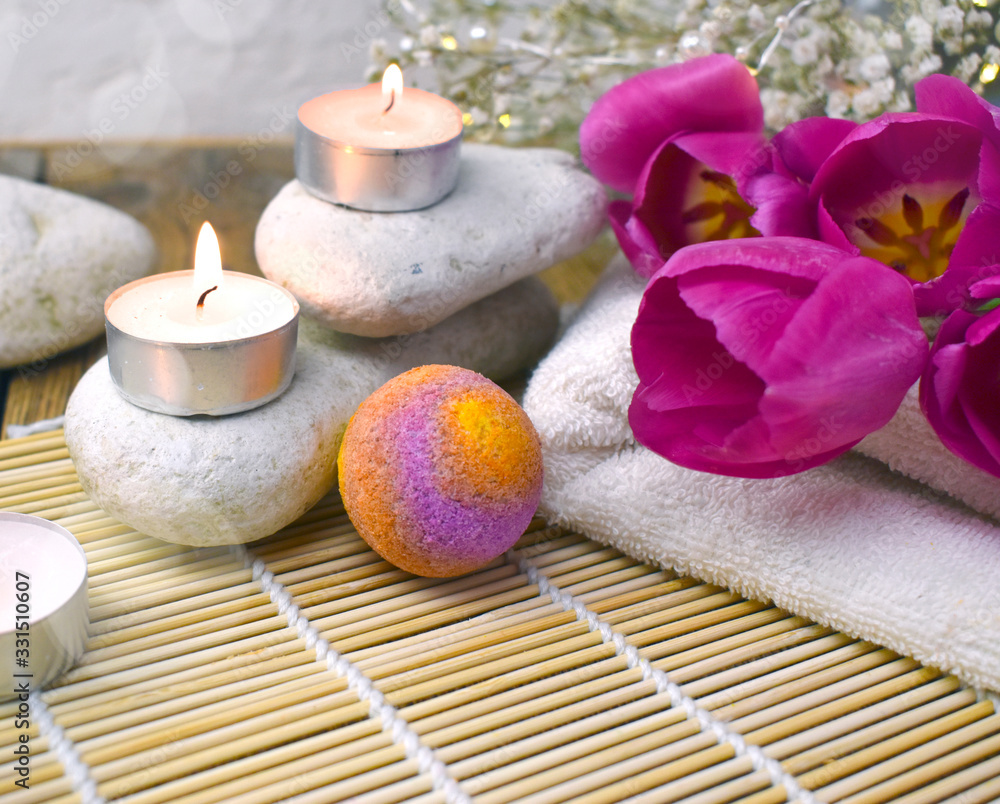 Close up spa composition with bath bomb, tulips, candles and pebbles on wooden background.  Resort concept for Valentines day, Mothers day or wedding greeting card.