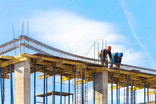 Two workers install a metal frame for a reinforced concrete beam
