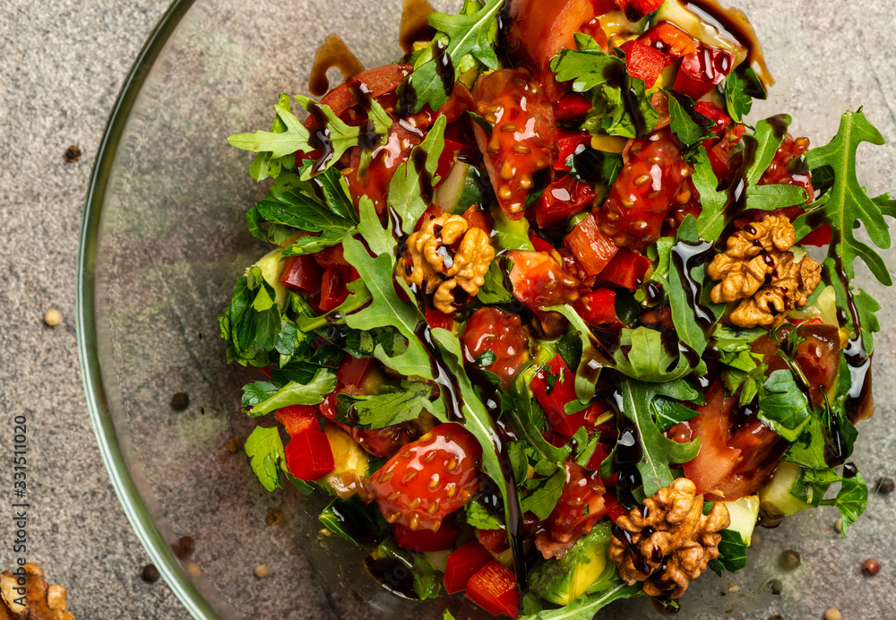 Vegetable salad with arugula, tomatoes, avocado, splashed with balsamic sauce in a glass bowl